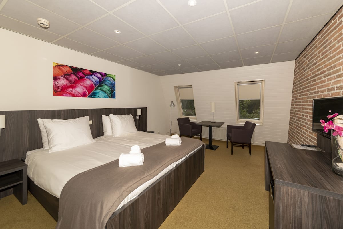 Ein Hotelzimmer mit einem großen Bett, einem Schreibtisch, einem Sessel, einem Fernseher und einem Gemälde an der Wand.