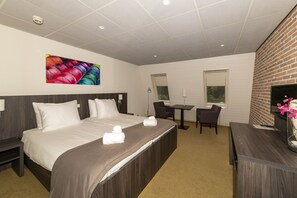 Una camera d'albergo con un letto grande, una scrivania, una sedia, una TV e un quadro appeso al muro.