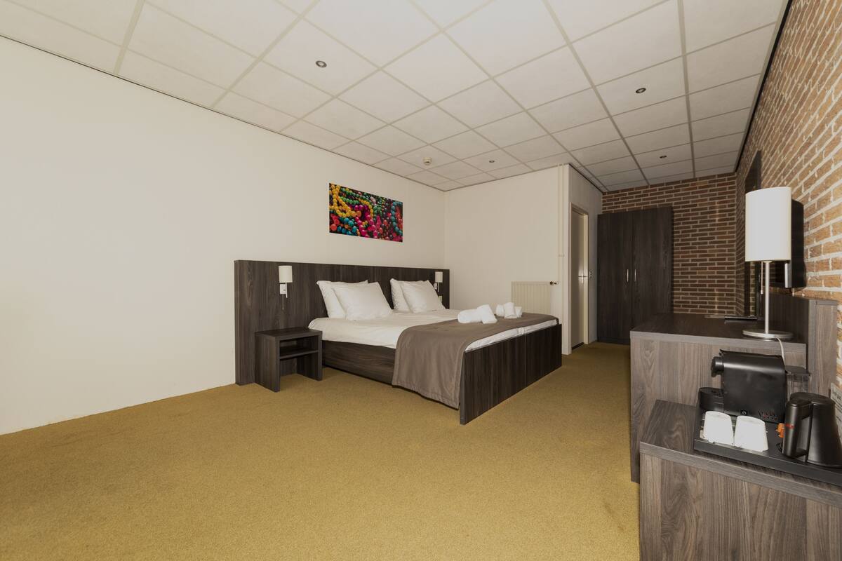 Ein Hotelzimmer mit Bett, Nachttisch und Schreibtisch mit Lampe und Kaffeemaschine.