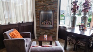 Un salon chaleureux avec une cheminée, des sièges confortables et une vue sur l’extérieur.