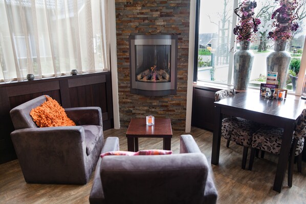 Un salon chaleureux avec une cheminée, des sièges confortables et une vue sur l’extérieur.