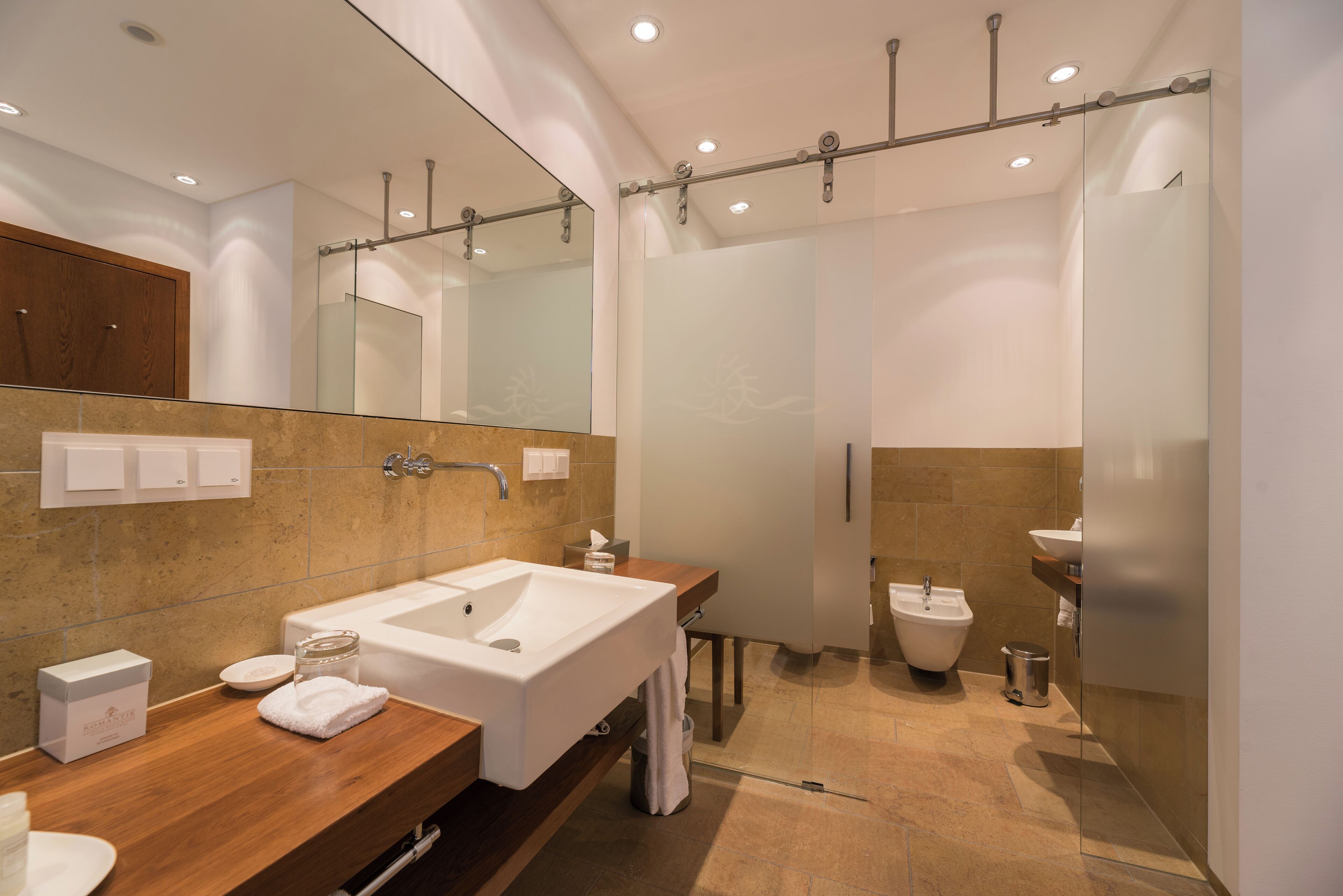 Un baño moderno con un lavamanos grande, un espejo y un área de aseo separada.