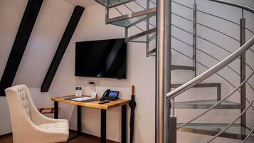 Ein modernes Zimmer mit Schreibtisch aus Holz, einem Sessel, einem Flachbildfernseher und einer Wendeltreppe.