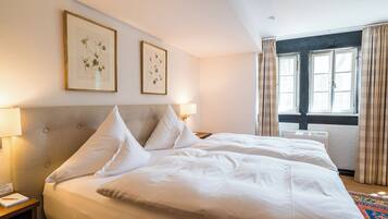 Une chambre d’hôtel avec deux lits, une grande fenêtre avec des rideaux et des reproductions encadrées de motifs botaniques accrochées au mur.