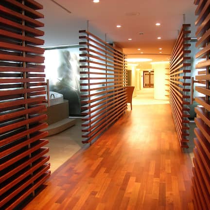 A modern hotel corridor with wooden slatted walls, a wooden floor, and a view of a spa area.