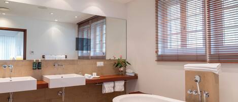 A modern bathroom with two sinks, a large bathtub, and wooden blinds on the windows.