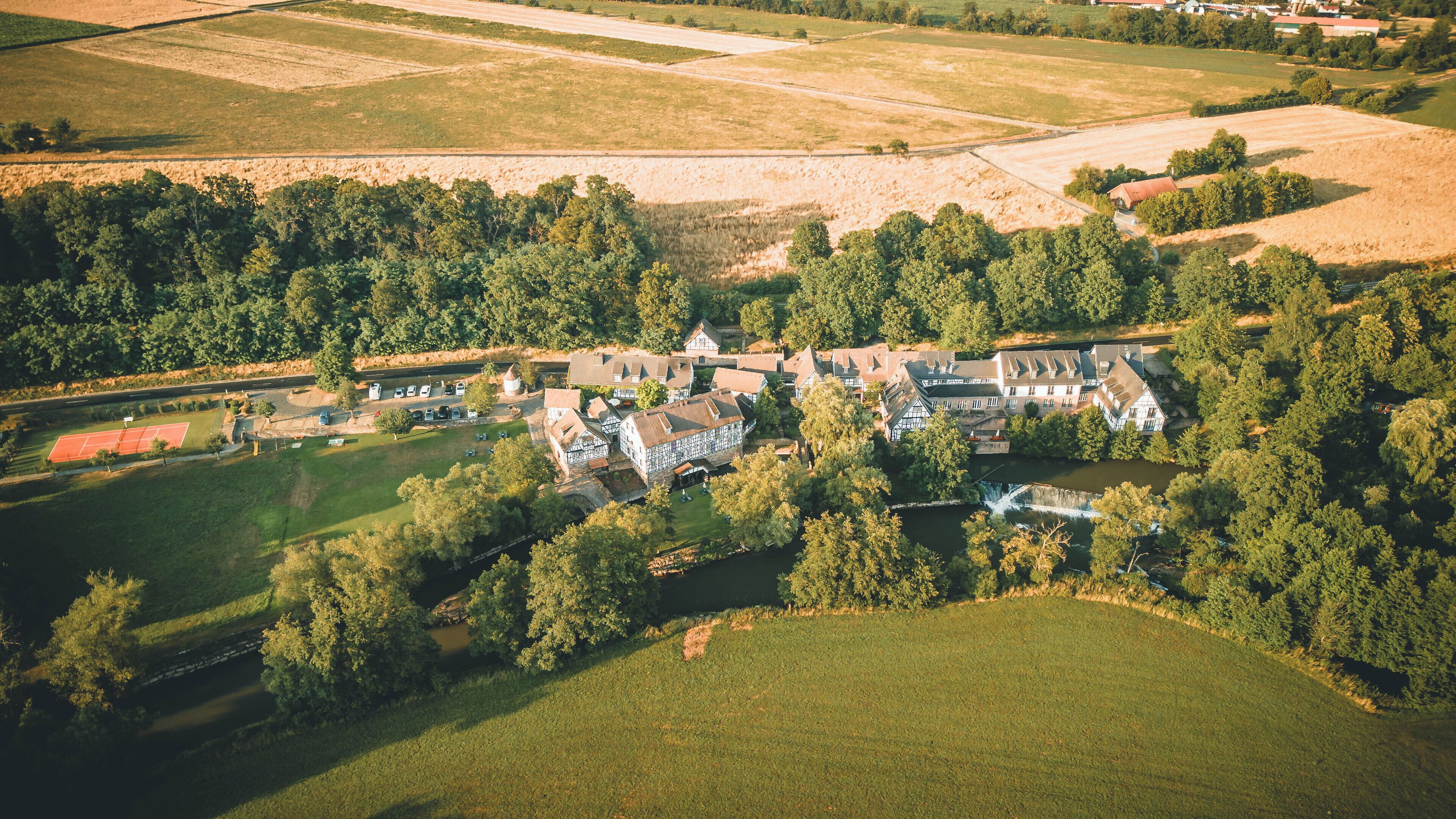 Vista aérea de una finca rural con una casa principal, varias edificaciones más pequeñas y una cancha de tenis.