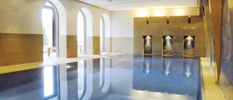 A large indoor swimming pool with clear reflections, arched windows, and a modern design.