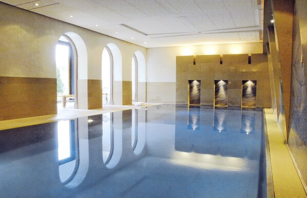 Una amplia piscina interior con reflejos nítidos, ventanales arqueados y un diseño moderno.