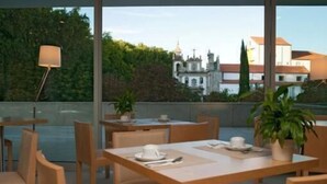 En tagterrasse med borde og stole, plantekasser og udsigt til en historisk bygning.