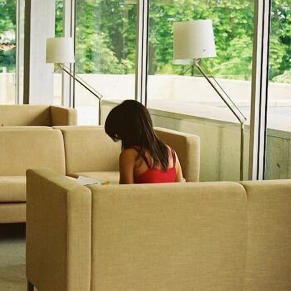 Una mujer sentada en un sofá beige en una habitación con ventanas amplias y lámparas de pie.