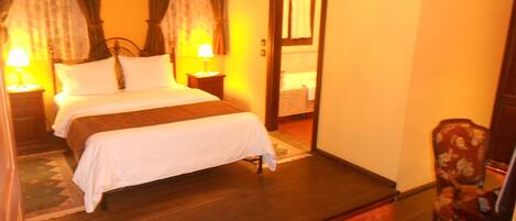 Habitación de hotel con una cama, dos mesitas de noche con lámparas, una silla y un espejo.