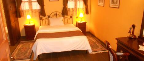 A hotel room with a bed, two bedside tables with lamps, a chair, and a desk with a mirror.