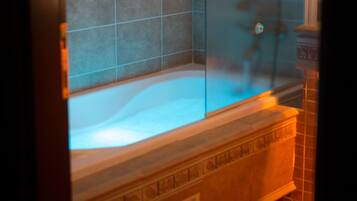 Un baño con bañera vidriada, paredes de azulejos y suelo de madera.