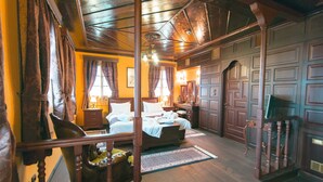 A traditional room with a wooden ceiling, a bed with white linens, a wooden chair, and a desk with a lamp.