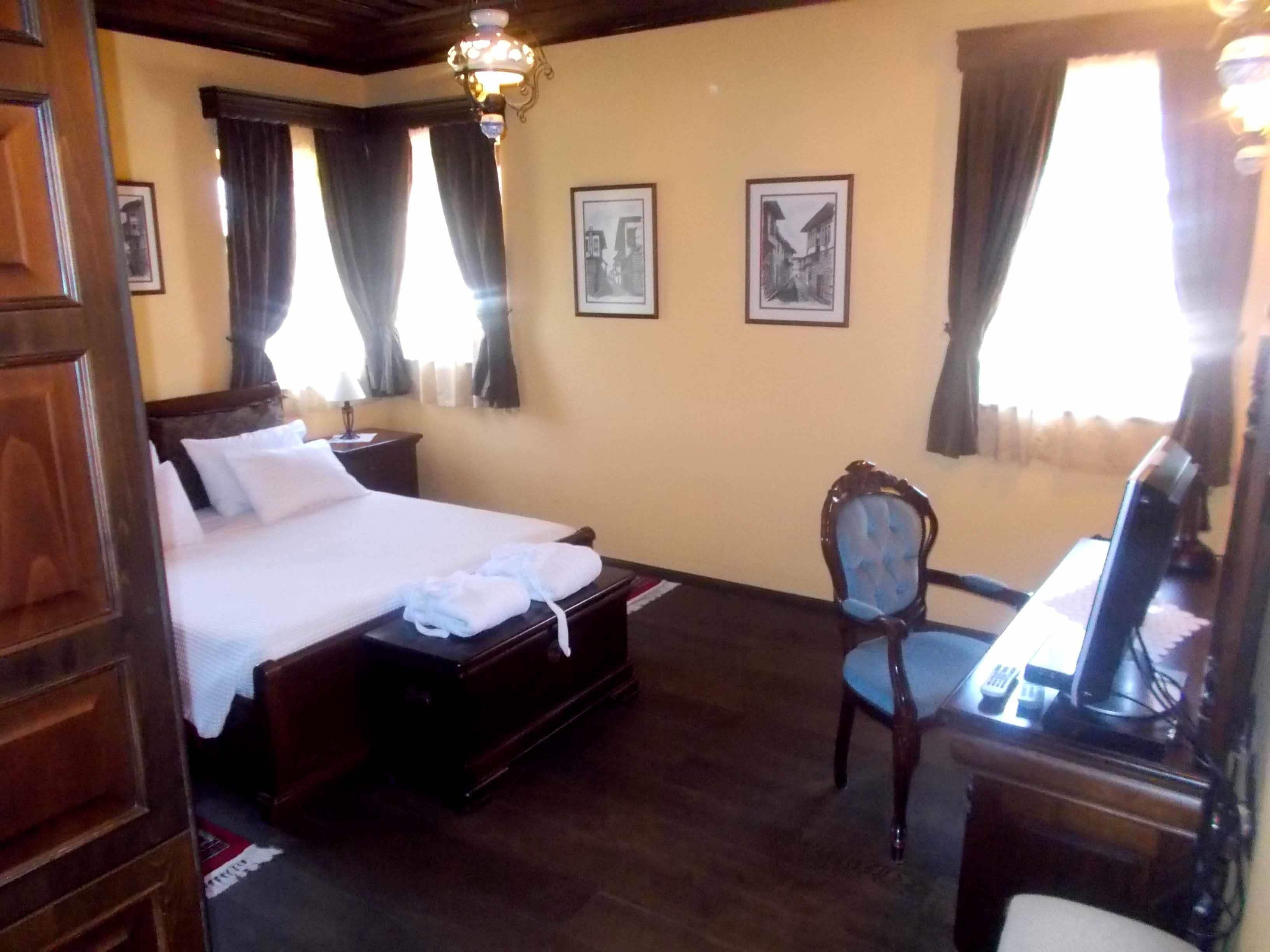 Habitación de hotel con una cama grande, un escritorio de madera, una silla y dos cuadros en la pared.