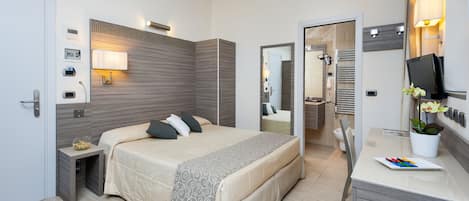 A modern hotel room with a large bed, bedside table, lamp, and a desk with a chair.