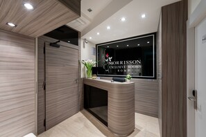 Ein moderner Empfangstresen mit einer Glastheke, einer Topfpflanze und einem Schild mit der Aufschrift 'MORRISON EXCLUSIVE ROOMS'.
