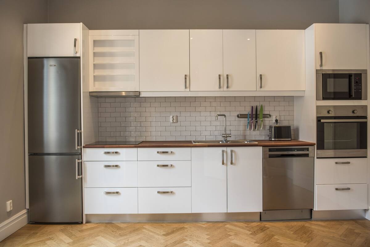 A modern kitchen with white cabinets, stainless steel appliances, and a herringbone wood floor.