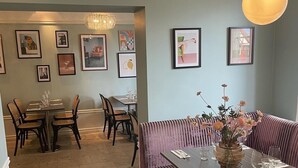 A dining area with a wooden table set for two, a cushioned bench, and framed artwork on the walls. - Donners Hotel (Visby)