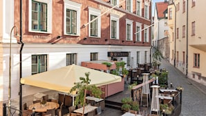 An outdoor café area with tables and chairs, a large umbrella, and potted plants. - Donners Hotel (Visby)