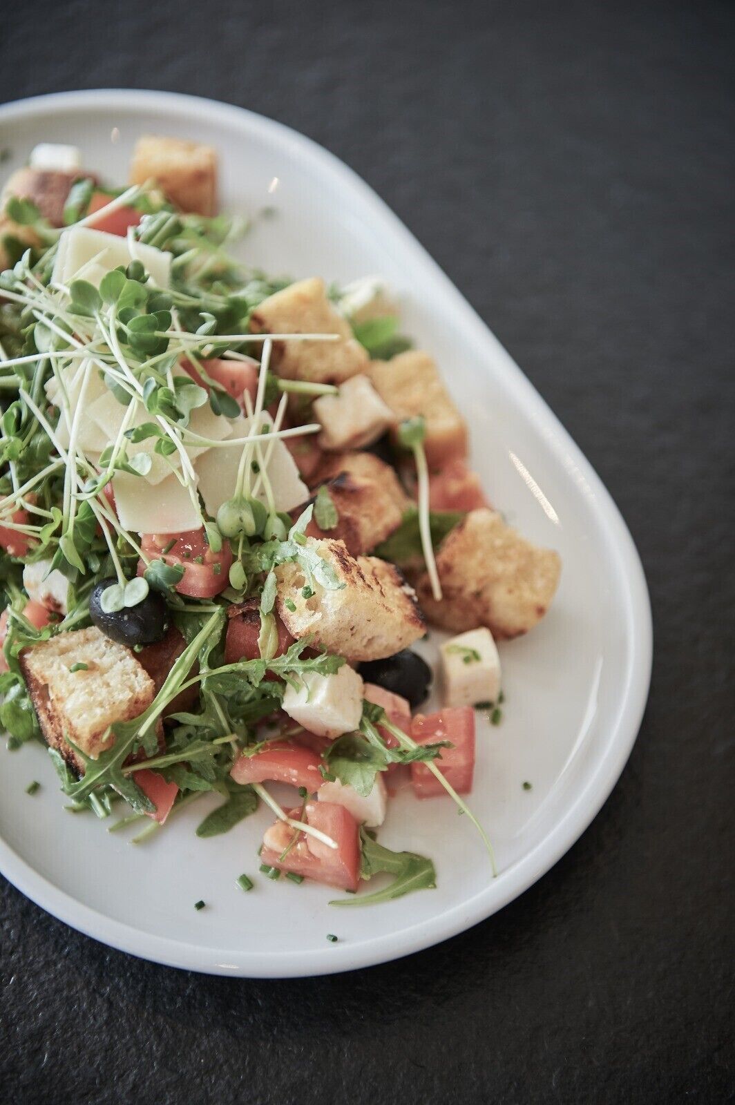 Un plato blanco con una ensalada de croutons, queso y vegetales verdes.