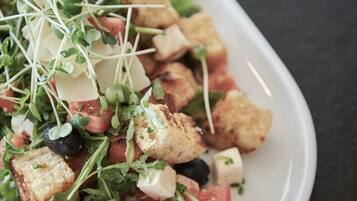 Un plato blanco con una ensalada de croutons, queso y vegetales verdes.