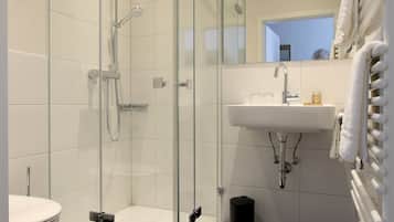 A modern bathroom with a glass-enclosed shower, a white sink, and a mirror.