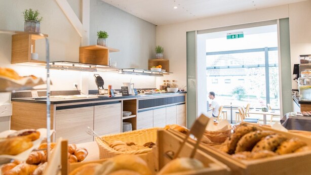 A modern cafe with a counter displaying pastries and a view of the street outside. - Adler Hotel & Gasthaus (Nonnenhorn)