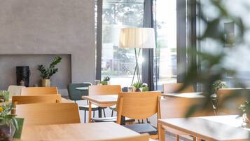 Una cafeteria moderna amb taules i cadires de fusta, plantes en testos i una finestra gran amb vista al carrer.