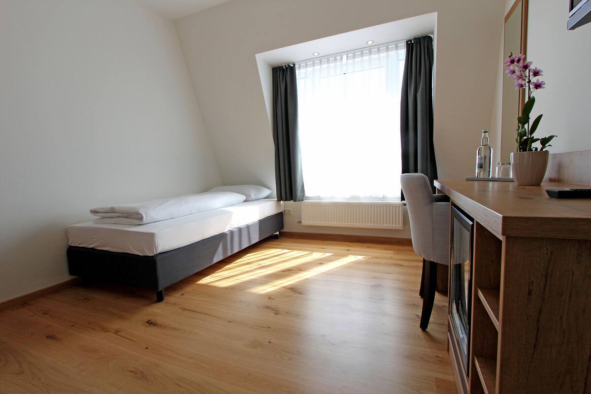A modern bedroom with a bed, a desk, and a potted plant.