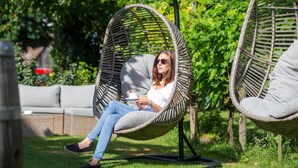 A wicker chair in a garden with a cushion, a grey cushion on a sofa, and greenery in the background. - Adler Hotel & Gasthaus (Nonnenhorn)