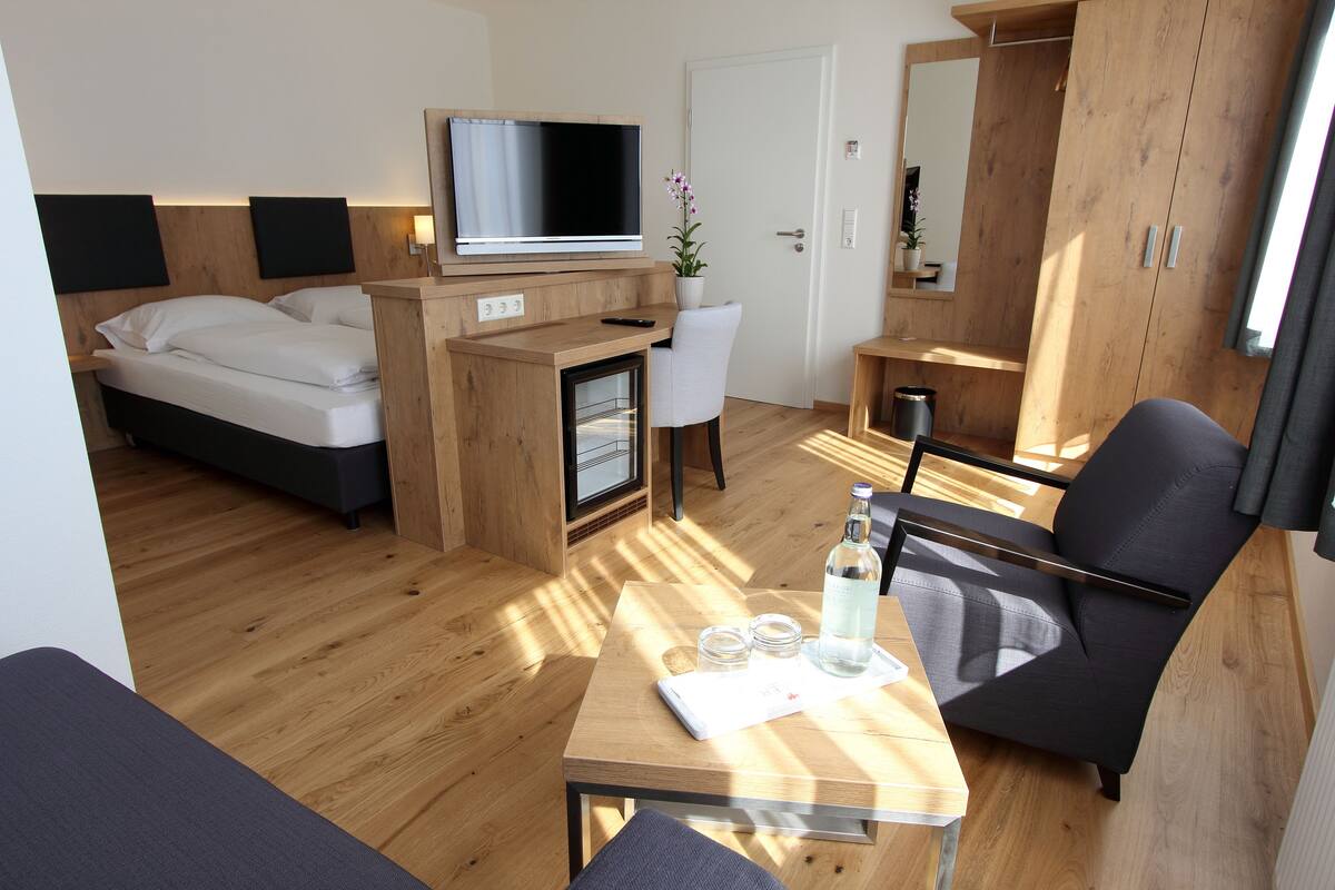 A modern hotel room with a bed, a desk with a TV, a chair, and a wardrobe.