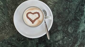A cup of coffee with a heart-shaped latte art on a white saucer, placed on a dark marble surface.