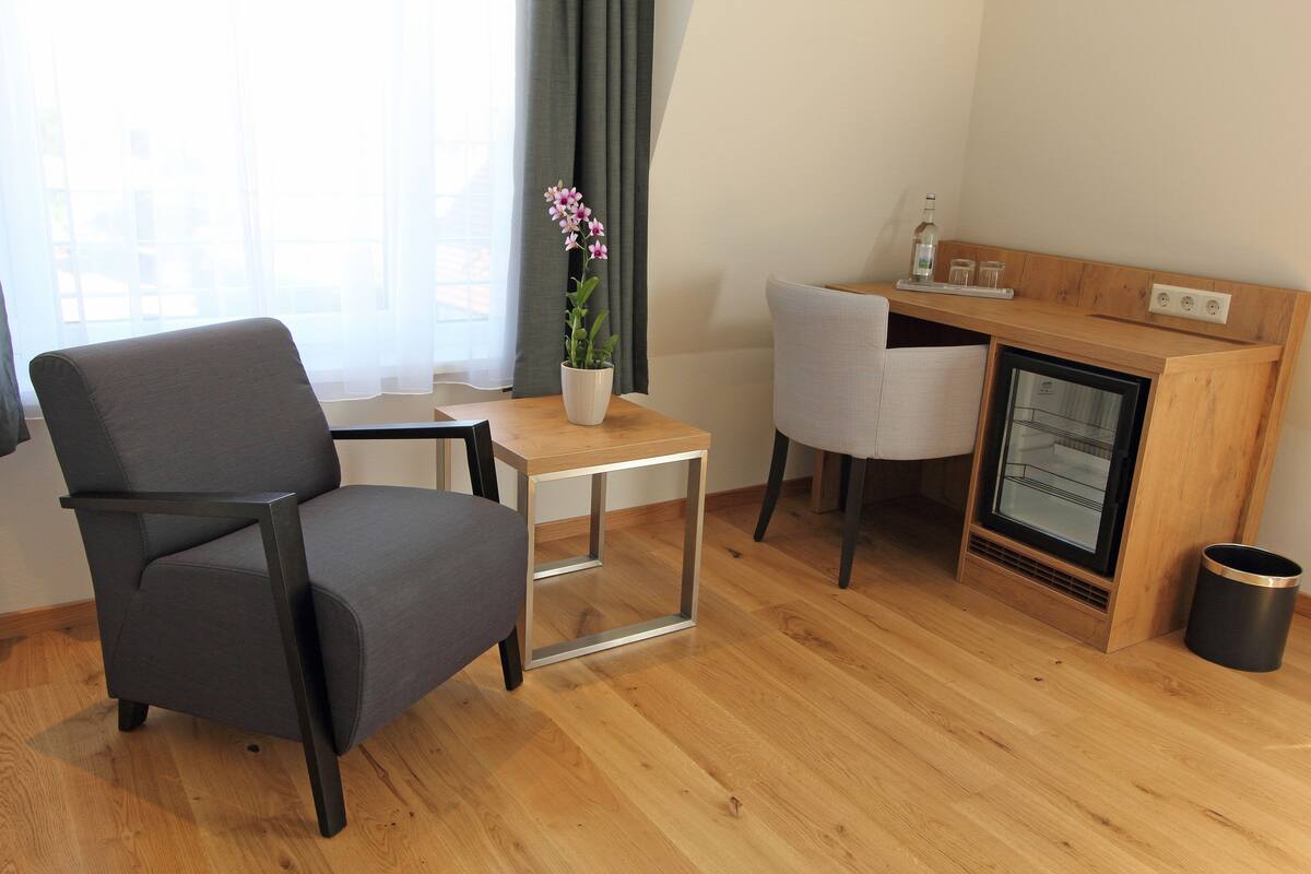 A modern room with a grey sofa, a small wooden table, a potted orchid, a compact refrigerator, and a trash bin.