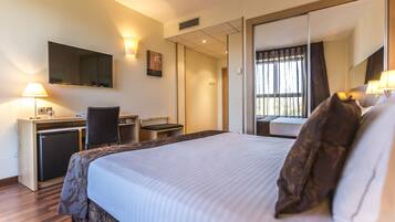A hotel room with a bed, desk, chair, TV, and a sliding door leading to a balcony.