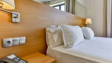 A hotel room with a wooden headboard, a bedside table with a telephone, and a lamp.