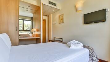 A hotel room with a bed, a desk, a chair, a TV, and a wall-mounted light.