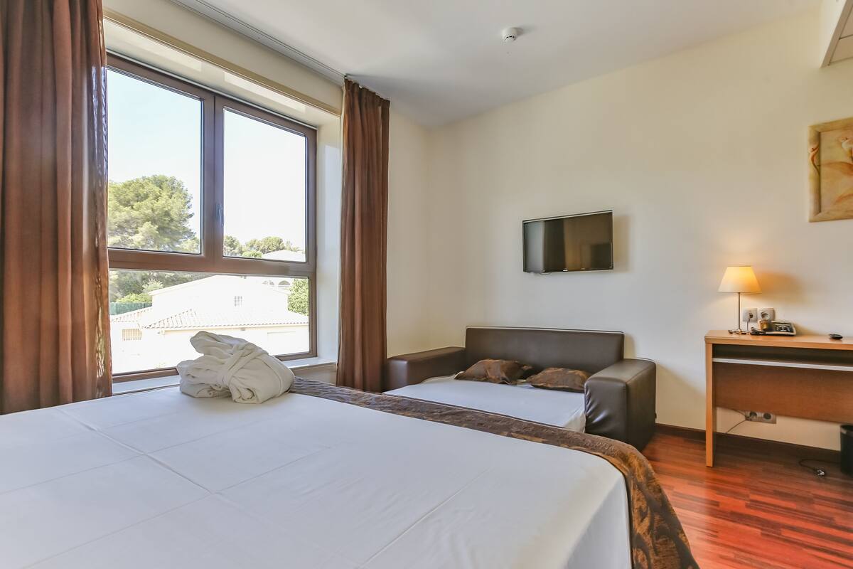 Quarto de hotel com uma cama grande, uma escrivaninha, uma cadeira e uma TV na parede.