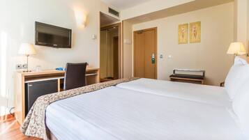 A hotel room with a large bed, a desk with a computer, a television, and a door leading to another room.