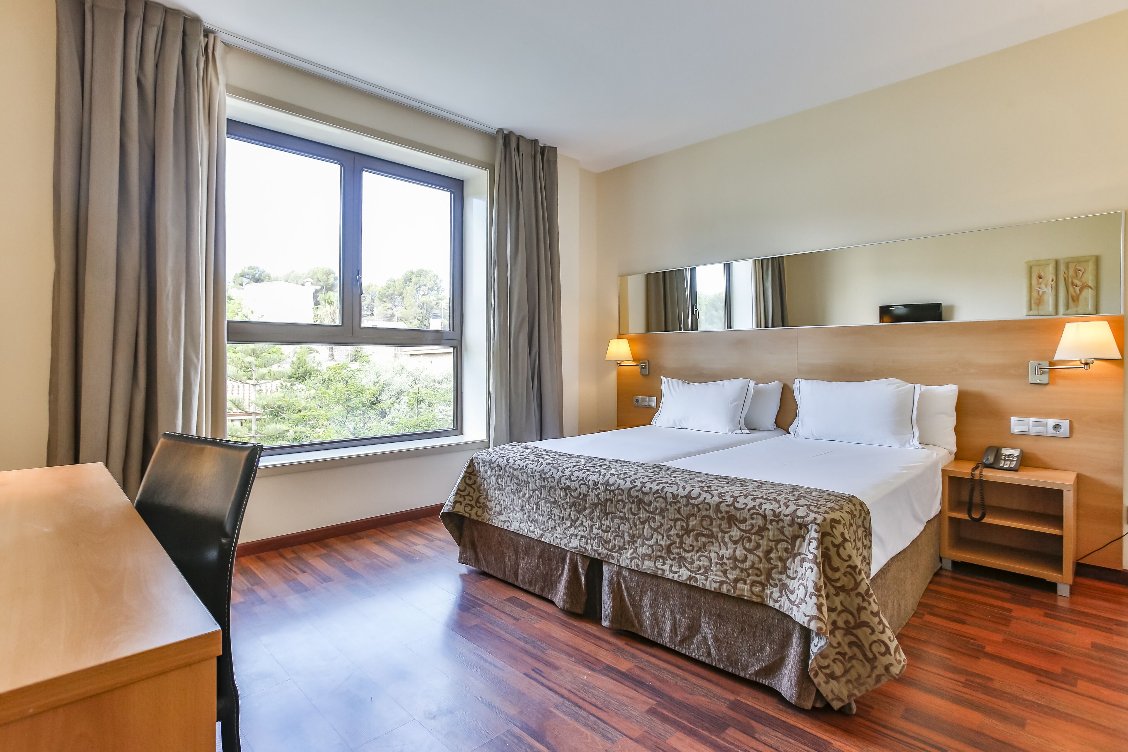 Habitación de hotel con una cama grande, un escritorio, una silla, una mesita de noche, una lámpara y una ventana con cortinas.