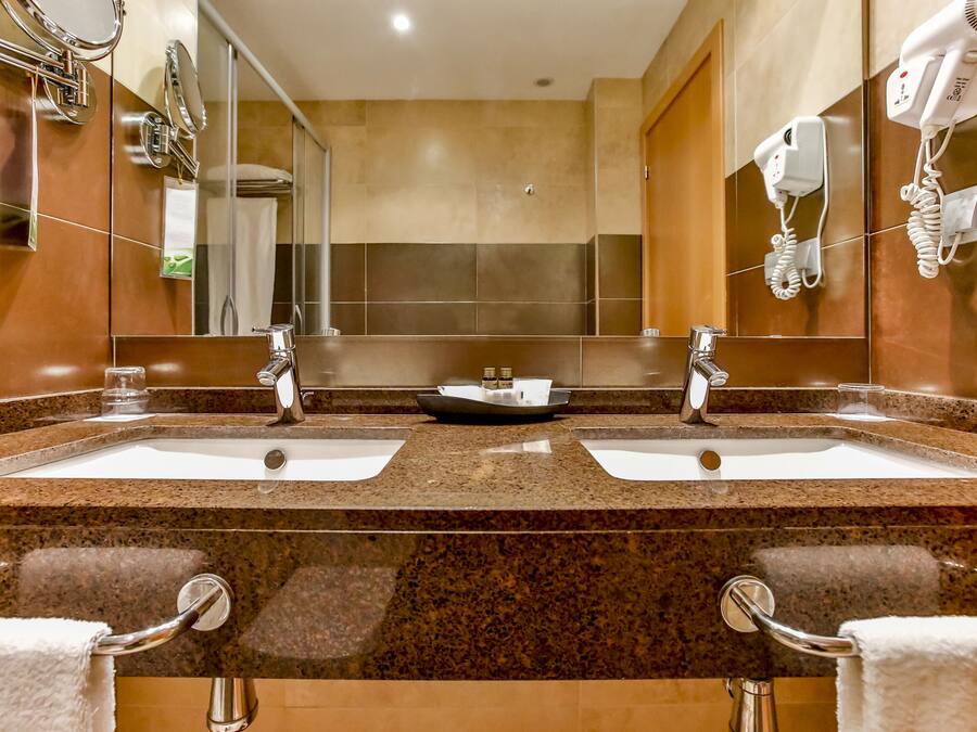 Un baño de hotel con dos lavamanos, un espejo grande y un secador de pelo en la pared.