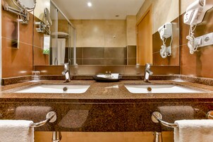 A hotel bathroom with two sinks, a large mirror, and a hairdryer on the wall.
