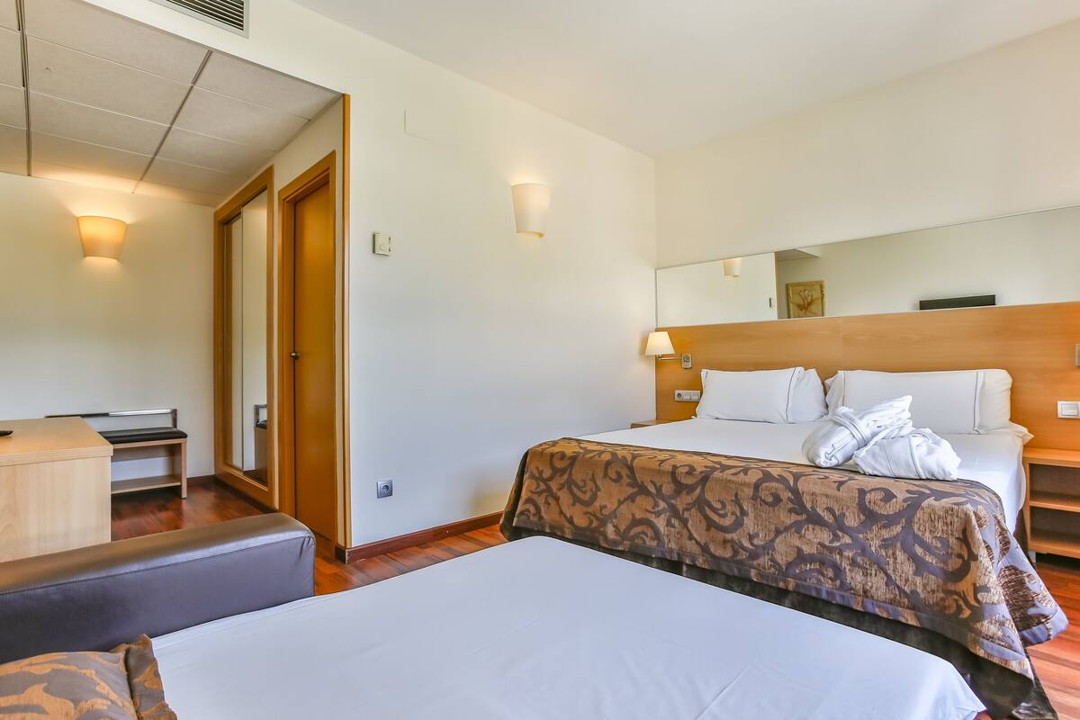 Quarto de hotel com duas camas, uma escrivaninha e um espelho.