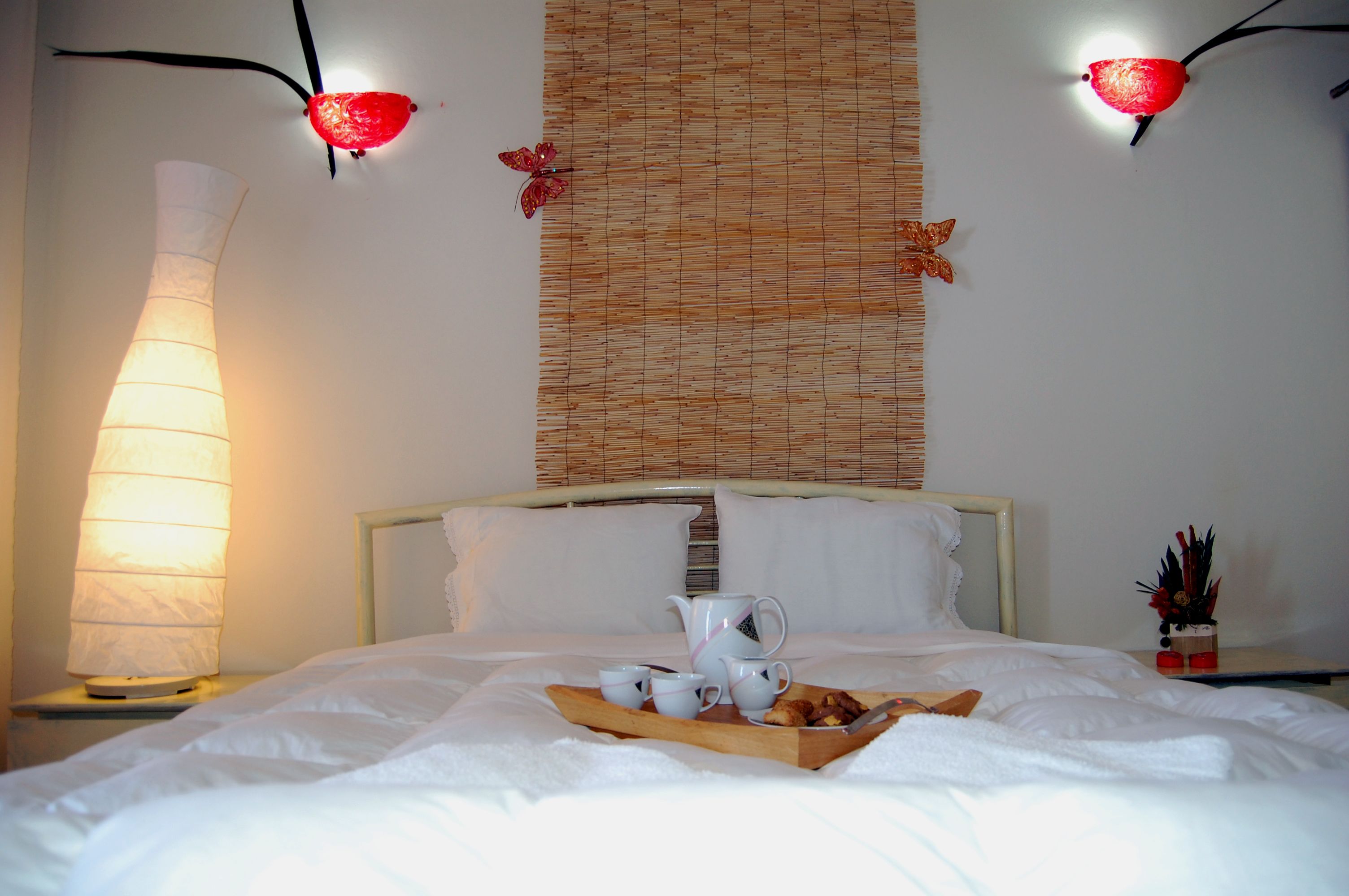 Un lit bien fait, avec du linge de lit blanc, un plateau contenant divers éléments pour le petit-déjeuner et un luminaire fixé au mur.