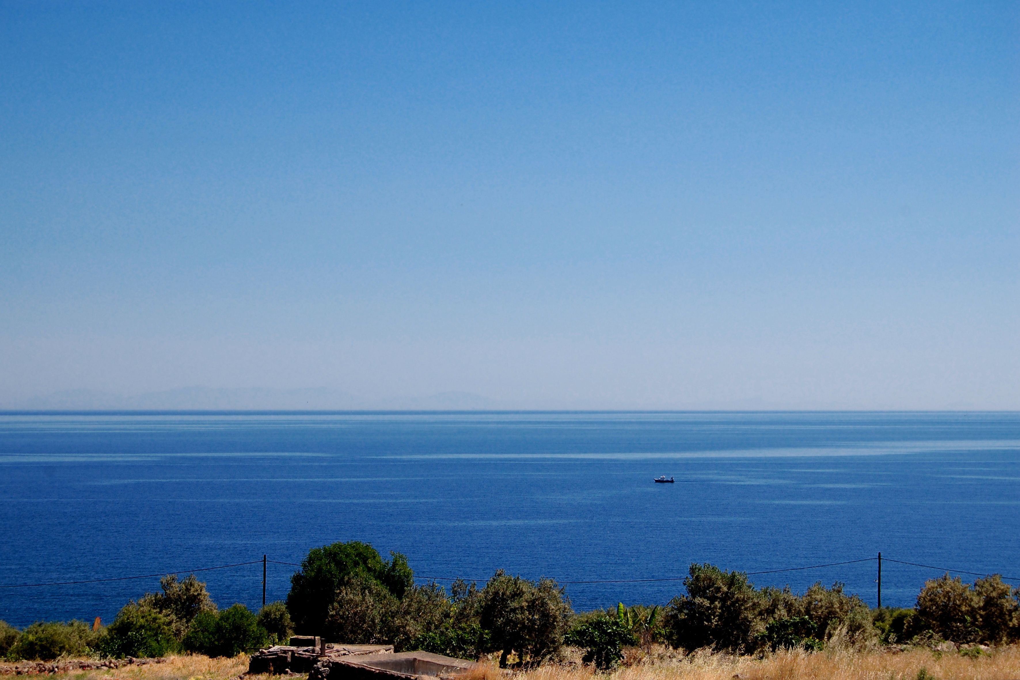 A coastal landscape with a clear view of the sea and distant mountains.