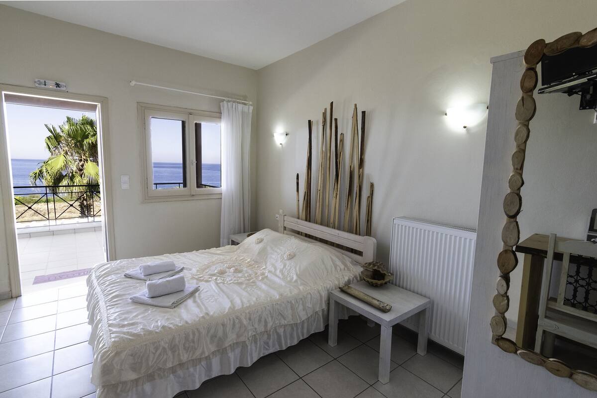 A bedroom with a bed, a nightstand, a window with curtains, a wall-mounted light, and a decorative wooden piece.