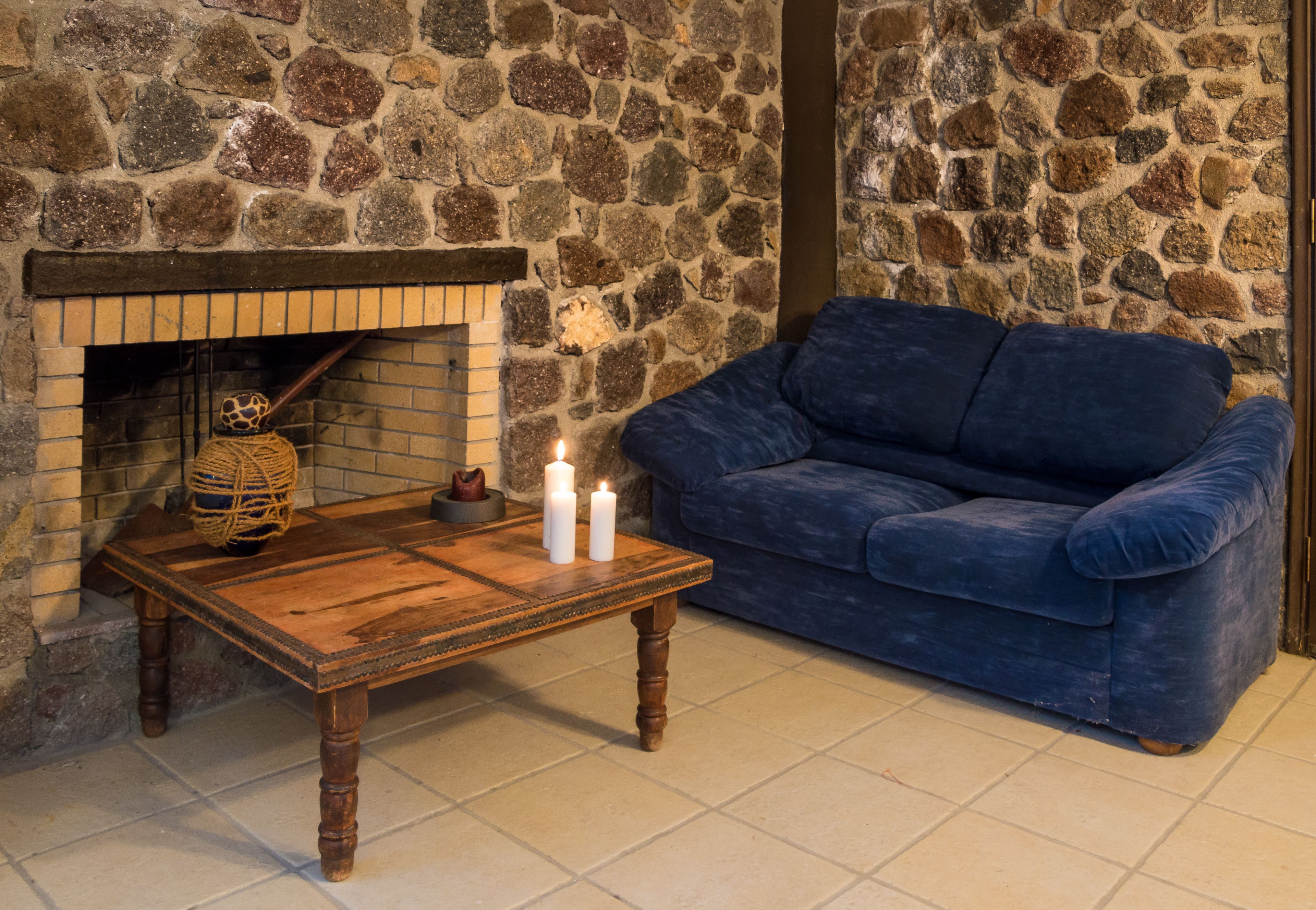 Un muro in pietra, un tavolo di legno con candele e un divano blu in una stanza.