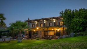 A two-story house with a balcony, outdoor seating area, and a stone wall. - Cavo Petra (Troizinia)