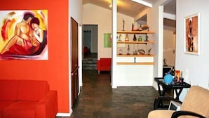 A modern living room with a red sofa, a beige armchair, and a coffee table with decorative items. There is a staircase leading to another room and a shelf with various objects. - Villa Flamboyan (Lauro de Freitas)